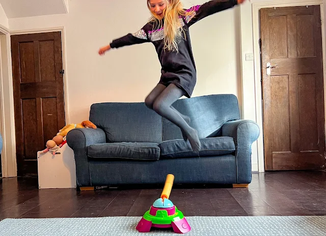 a girl jumping  high over a rotating boom arm in the living room