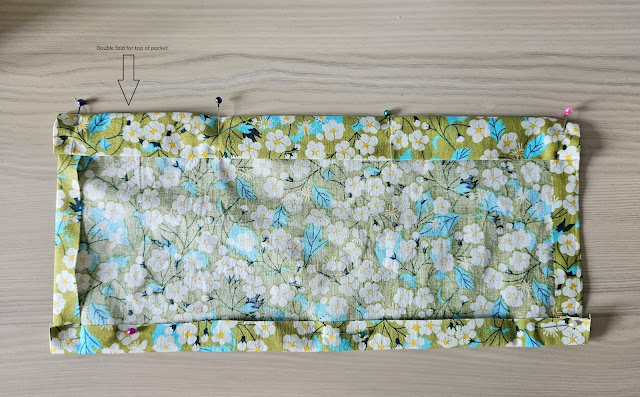 rectangle of green floral fabric showing fold lines for pocket edging