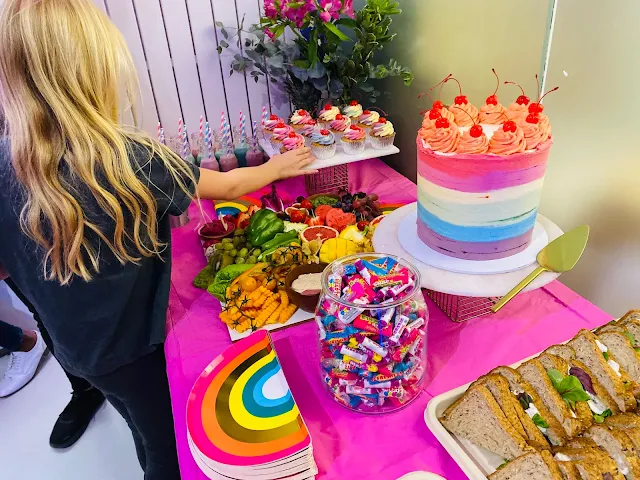 An 8 year old reaching for a cupcake on a buffet table with rainbow plates, lots of fruit, sweets and sandwiches