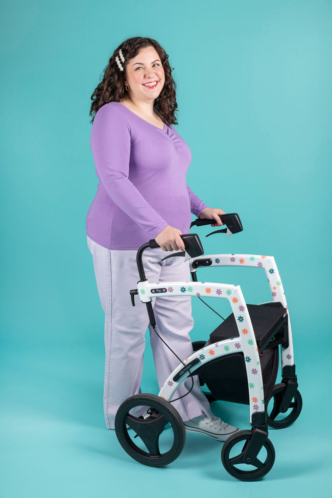 Model with brunette curly hair holding mobility aid walker wears purple long sleeve jersey top with sweetheart neckline