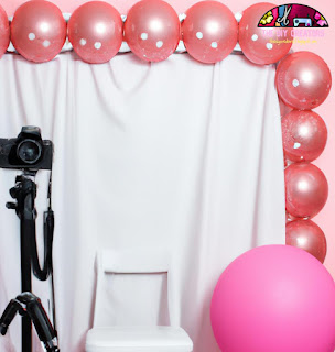 DIY photo booth with a pink backdrop, balloons, and a camera on a tripod