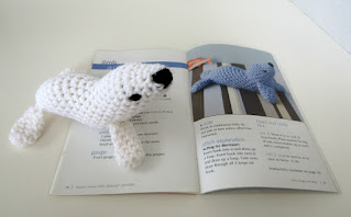 Toy seal looking at the pattern for him in the crochet pattern book