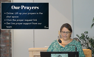 A white woman with glasses at the lectern sharing prayers with a visual slide in the upper right corner.