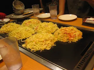 Okonomiyaki batter being cooked on a flat top grill in the middle of a dining table