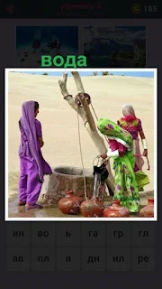 две женщины поднимают воду из колодца и наливают в кувшины