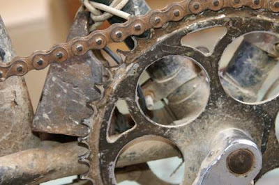 image of a Chinese bike, close focus on the major chain wheel, with a small weight affixed to the shaft by a wire.