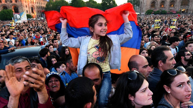 Picture of A girl holding The Armenian flag on a man's shoulders  with a protesting crowd in the background