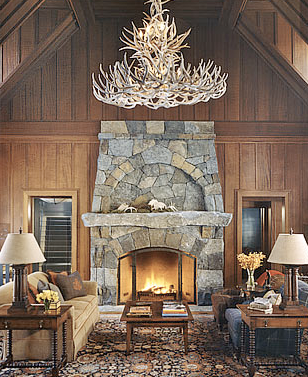 Wood paneled living room with vaulted ceiling, an antler chandelier and stone fireplace and mantel by Peter Pennoyer