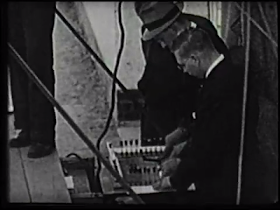 A black and white photograph of two men bent over a switchboard.