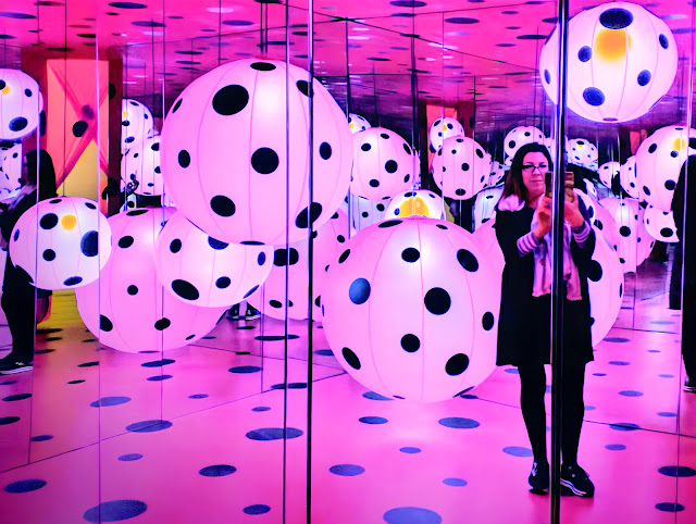 This is a photo of visual artist Dawn Hunter at the Yayoi Kusama exhibition at the High Museum in Atlanta, GA. Dawn is standing in a hot pink room with big black polka dots created by Kusama.