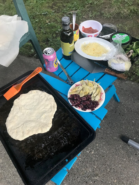 pizza dough on cookie sheet on small table, with dishes of topping on another small table