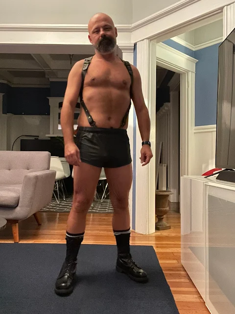 Sporting leather shorts and suspenders a hairy bearded daddy bear smokes a cigarette