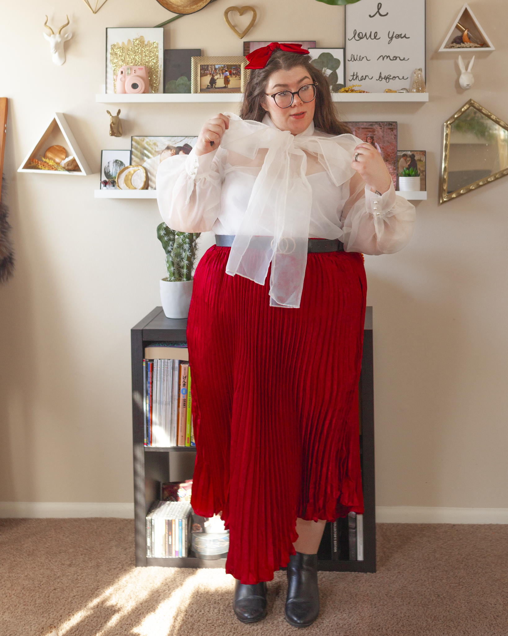 An outfit consisting of a white sheer long sleeve blouse with a connected pussy boy tied into a bow around the neck, tucked into a wine colored pleated maxi skirt and ankle boots.