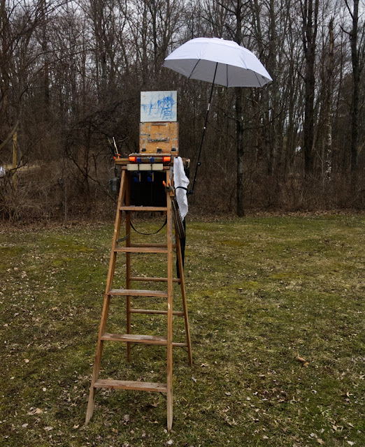 Stepladder with pochade box mounted on extension to top step. A sketch in blue paint is in progress. An umbrella is attached to the side of the ladder