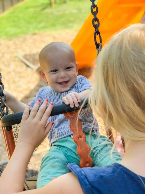 baby boy being pushed on a swing by his biggest sister. He is smiling