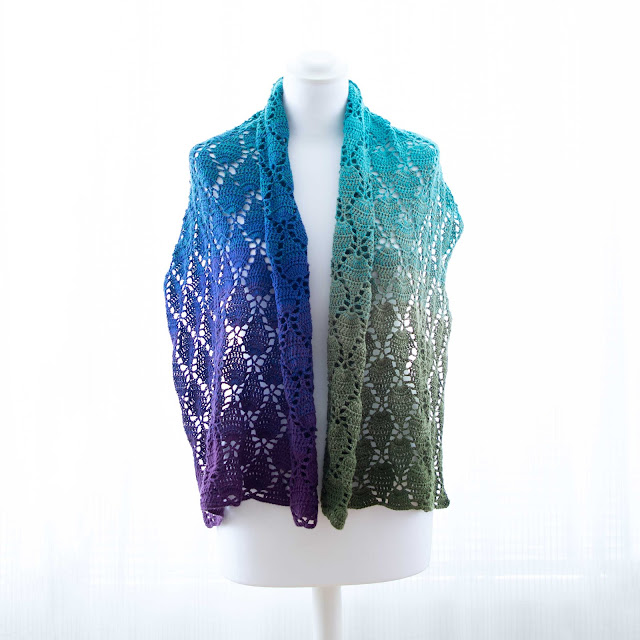 Broad rectangular crochet shawl inspired by peacockfeathers. Stitch pattern looks like little plumes in variegated yarn from purple to blue to aqua to green
