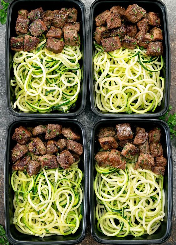 overhead photo of four meal prep containers with Garlic Butter Steak Bites with Zucchini Noodles