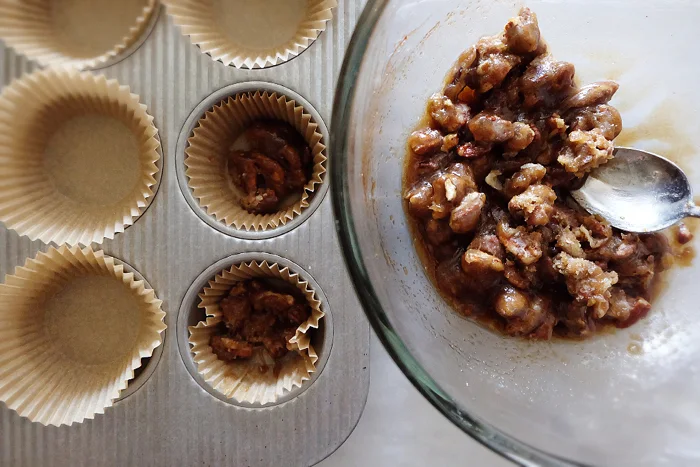 adding pecan topping to muffin cups in tin