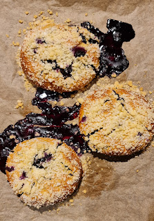 Three jagodzianki on a baking sheet, after baking, with pools of blueberry juice having leaked out during baking.