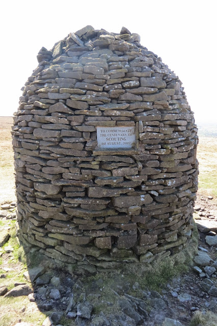 A photo of the cairn, a cylinder tapering to a narrow point at the top, with a plaque commemorating the centenary of the Scouts.