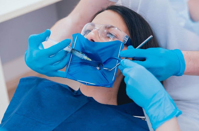 il dentista sta iniettando un ago per anestesia in una donna sulla cinquantina per lavorare sul suo dente anteriore