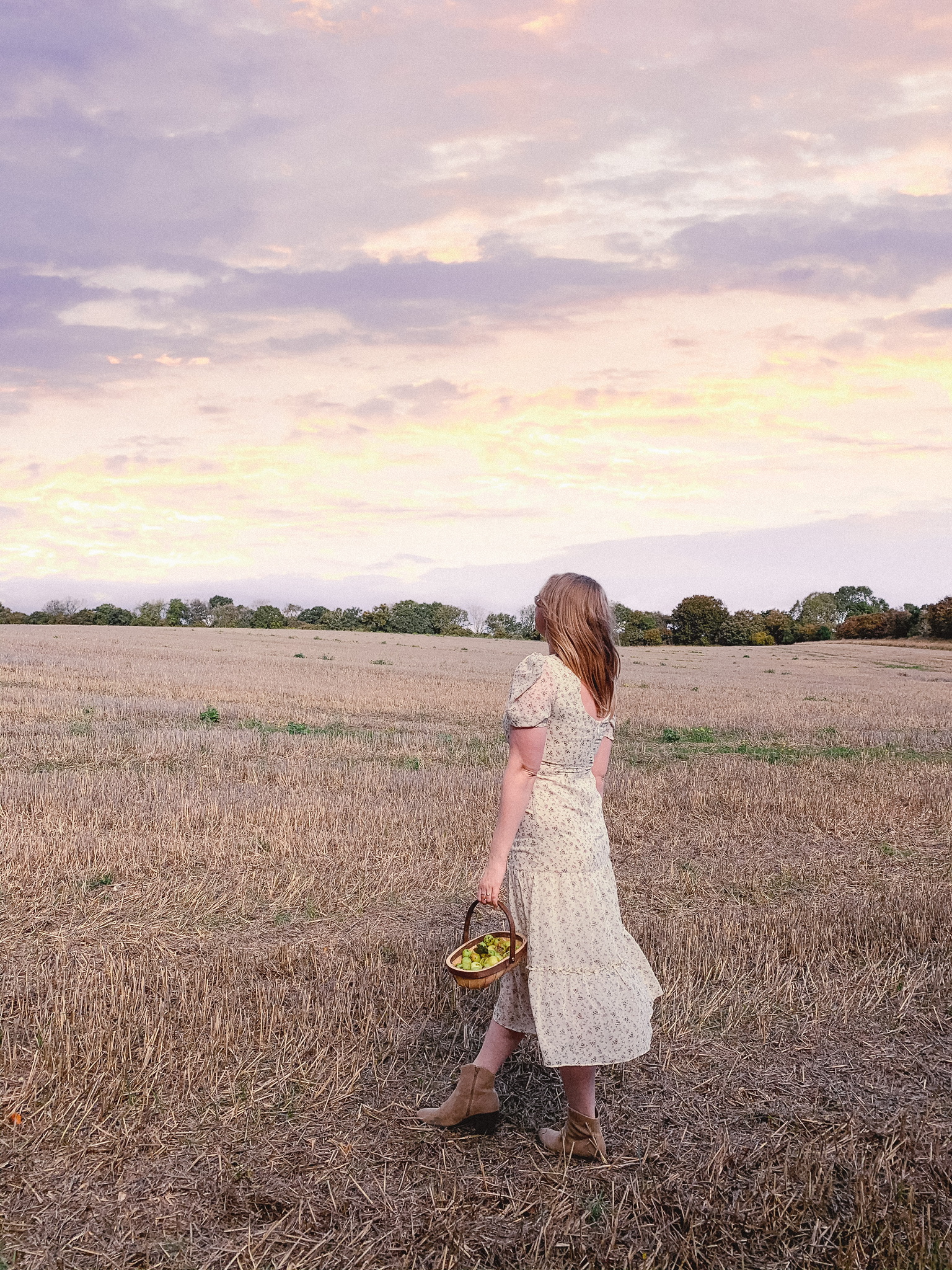 Fashion blogger standing in a Hampshire countryside field looking at the sunset