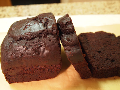Two slices of dark chocolate cake lying next to a loaf of chocolate cake