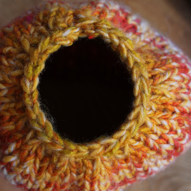 Top view of the hole on the top of a knitted yellow and rainbow beanie. Hole is for a ponytail or bun.