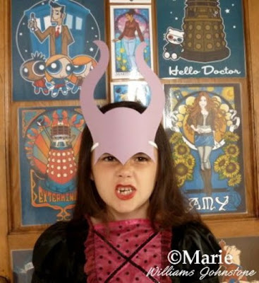 Girl wearing a purple paper mask of elasticated horned head piece in witch costume dress
