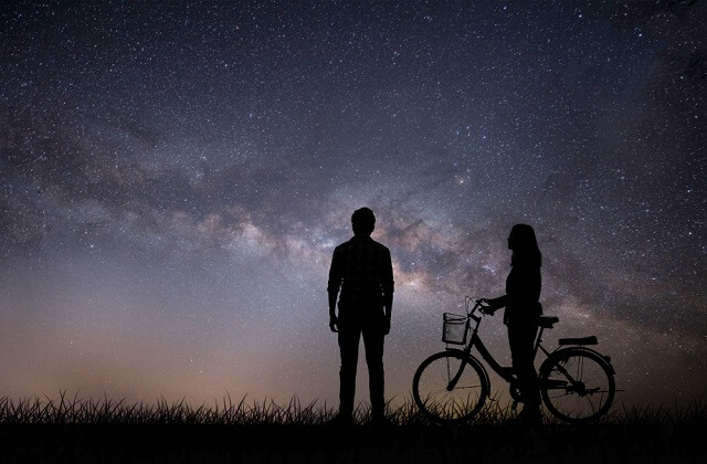 man standing and woman on a bicycle watching the stars on the horizon