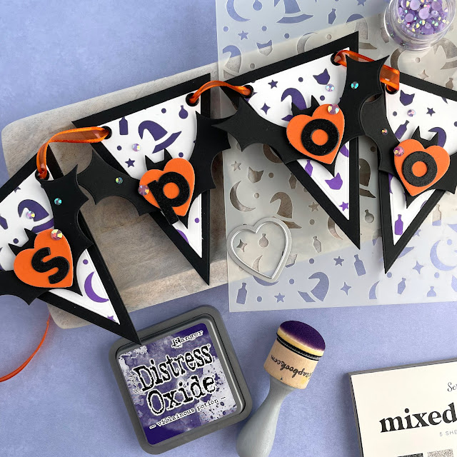 Spooky Halloween Banner created with: Scrapbook.com halloween bats die, magic potion stencil, glitter paper metals, smooth cardstock rainbow, domed foam blending tool, nested hearts, bold basic alpha, nested triangle banner; Tim Holtz distress oxide villainous potion, wilted violet; Pinkfresh jewels