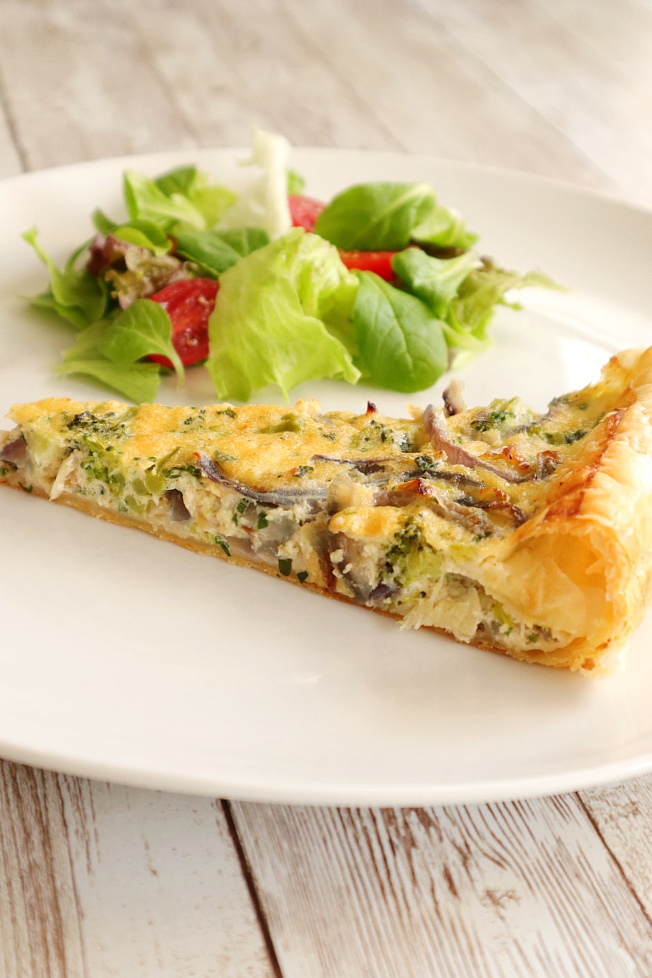 slice of codfish and broccoli tart on a plate with tomato lettuce salad