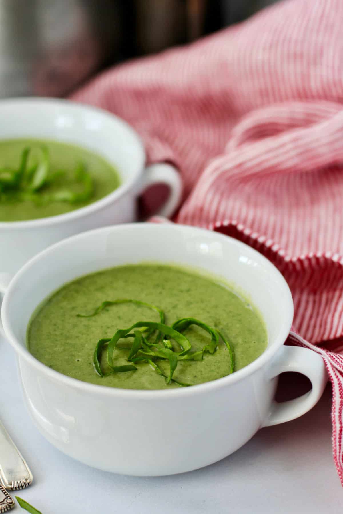 Cream of spinach soup in two bowls topped with spinach pieces.