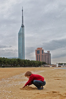 child on a beach with a glass skyscraper behind