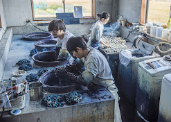 Three people hand dyeing indigo in China. The two on the left are reaching into vats full of blue liquid.