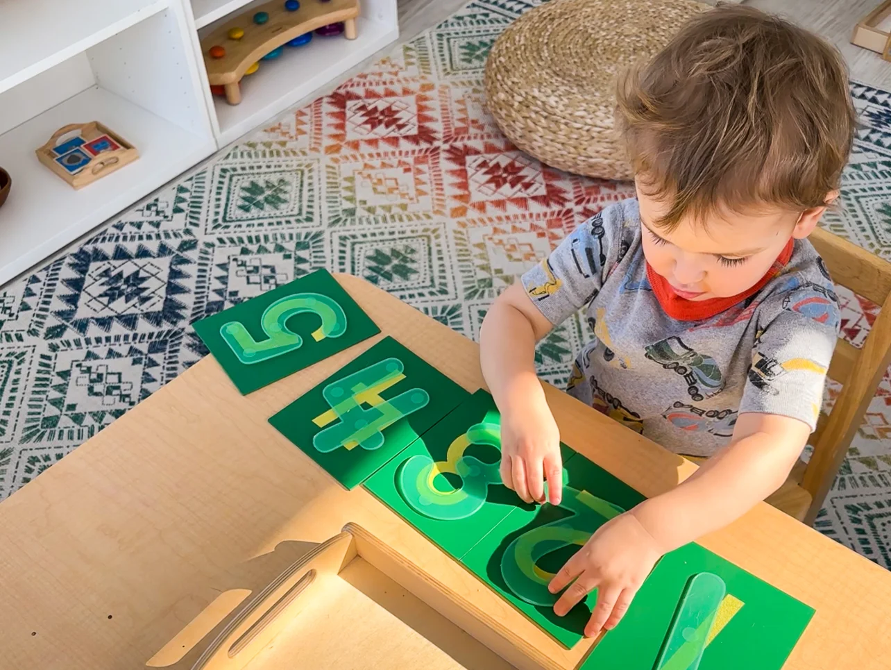 Three-year-old Montessori preschooler places silicone number toys over Montessori sandpaper numbers as he learns to count.