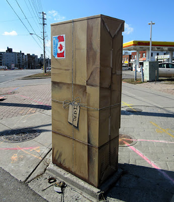 Traffic signal box painted to look like a parcel wrapped in brown paper and string.