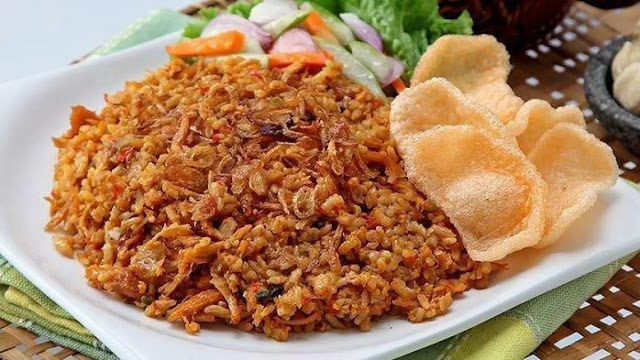 Plate of Indonesian Malang-style fried rice with sliced sausage, chicken, egg, and prawn crackers, served with cucumber and tomato.