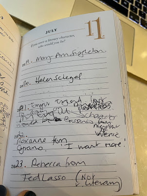 The page from July 11th of a 5 year diary. The question at the top says, If you were a literary characters, who would you be.' There are five years of entries. The top line says, '2019. Mary-Anne Singleton.' The next line down says, '2020. Helen Schlegel.' The next line down, in really messy, hard-to-decipher writing, it says, '2021. Tonight England lost to Italy on penalties. My Eng Lit character would be Bassanio from the Merchant of Venice.' There are scribblings out and arrows to show missing words. It's a hot mess. The next line underneath that, in neat writing once more, says, '2022. Roxanne from Cyrano. I want more.' Then the final line at the bottom of the page says, '2023. Rebecca from Ted Lasso. (Not very literary.)'