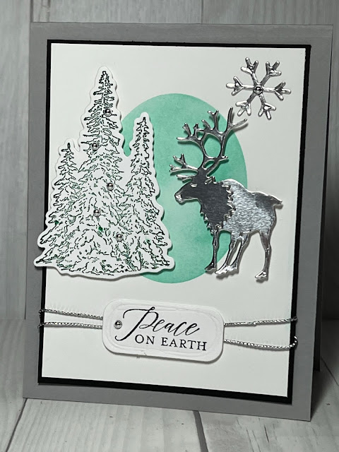 Silver foil Reindeer standing next to a Christmas Tree with a Christmas Sentiment