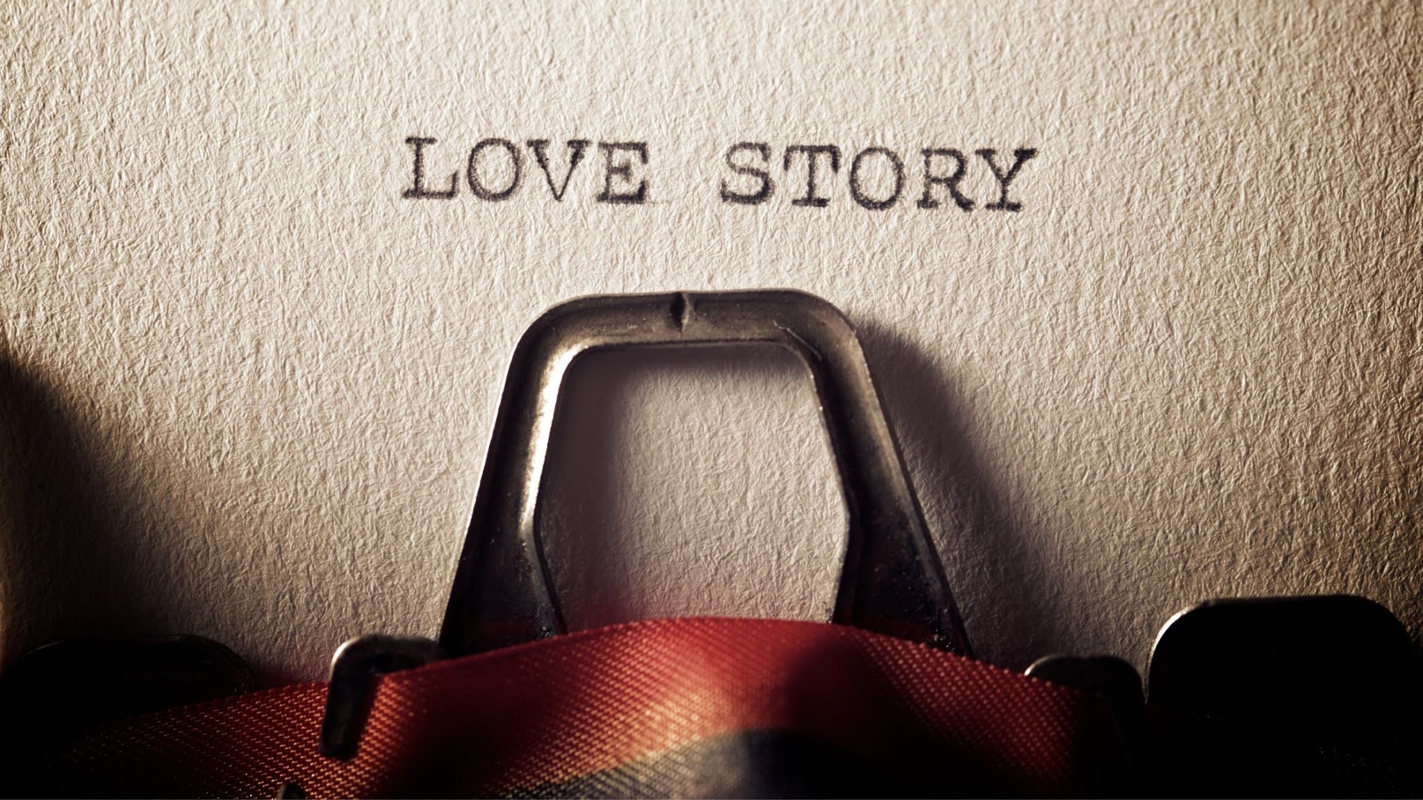 page of texured paper in a typewriter. The words "love story" have been typed on the page.