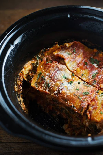 Image is a black crock from a slow cooker, filled with a vegetable lasagna with melted cheese on top. One slice is missing.