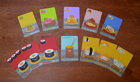 A display of the various cards available in Sushi Go. In the top row is Wasabi, Sashimi, Tempura, Pudding, and Dumplings. The bottom row has three Maki Roll cards, which are identical except one has a single Maki Roll icon, another has two icons, and the last has three. Next to these is the Chopsticks, followed by the three Nigiri cards: Egg, Salmon, and Squid. All of these cards are a different colour, except all the Maki Roll cards are red, and both the Nigiri and Wasabi cards are yellow. The art on each card is a cute cartoon-character rendition of the sushi item represented by that card (for example, the Dumpling card shows a happy little Dumpling with a cartoon face.
