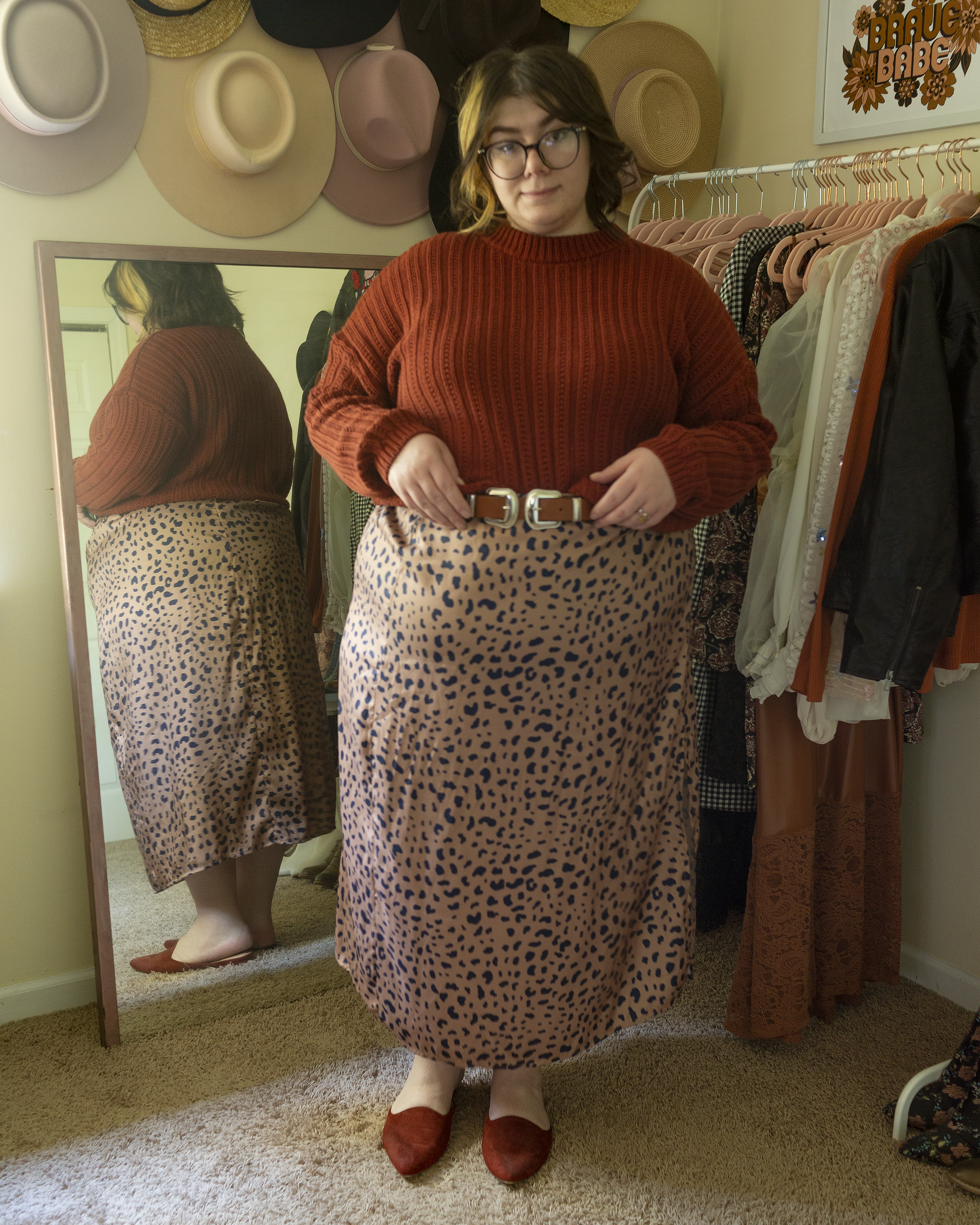 An outfit consisting of a burnt orange cable knit sweater half tucked into a tan and navy blue animal print satin slip skirt and burnt orange mules