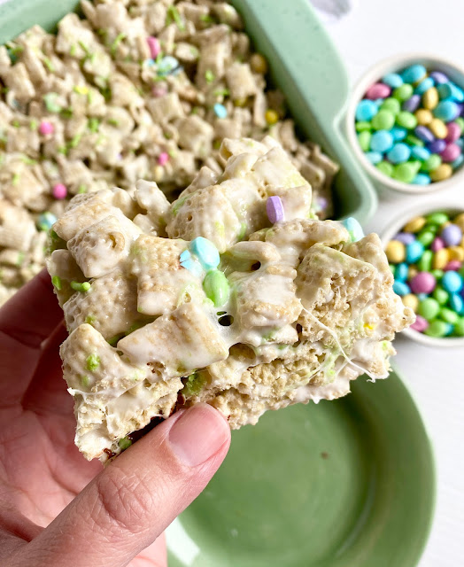 Hand holding a cereal bar with bowls of candies in the background.