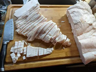 A thick slab of pig fat on a cutting board, being diced into small pieces.