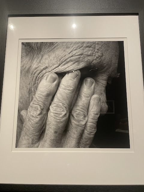 This is a picture taken of an old woman with her hand up to her face. She seems in distress. She is very, very wrinkly. The photo was taken in black and white.
