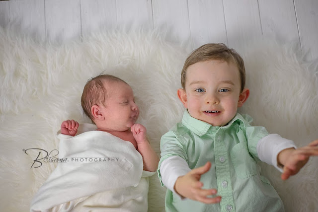 toddler lying with newborn baby sibling on white rug