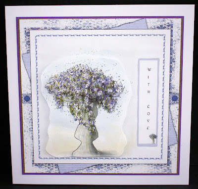 Image is a photo of a multi-layered hand-crafted card, featuring a watercolour drawing of a formal stone garden planter, festooned with small purple flowers.