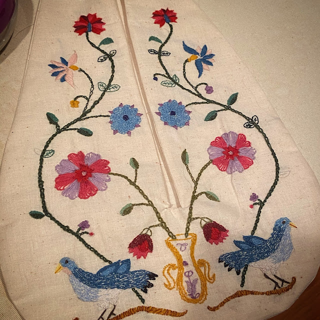 photo of the finished pocket on natural undyed cotton with colorful flowers, vines, and blue birds embroidered on it